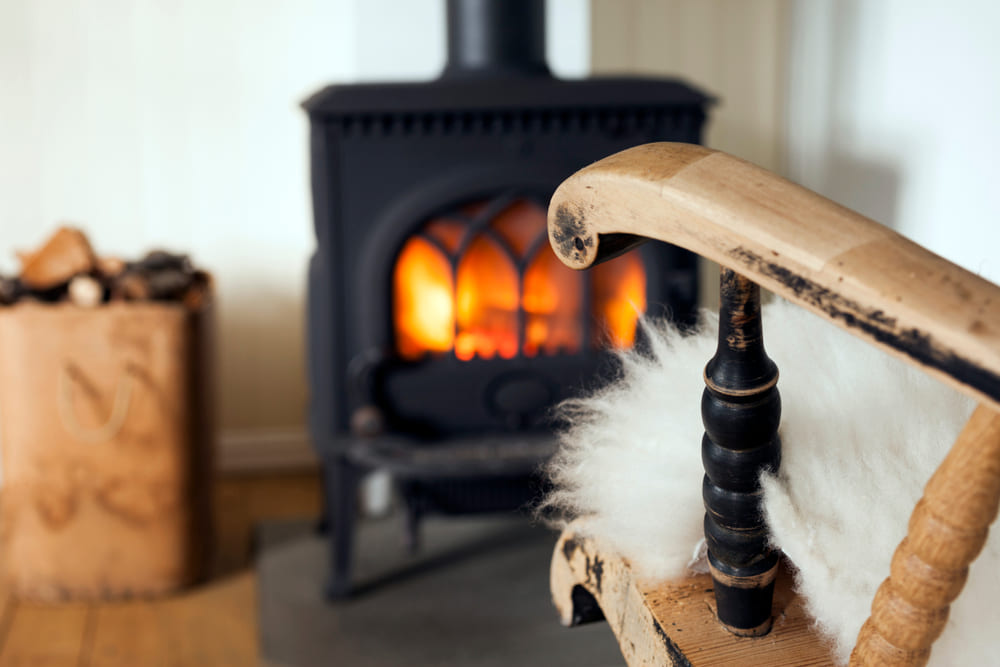 Warm and cozy corner in Scandinavian country house: wood burning stove, box of firewood and old restored rocking chair. Shallow focus on armrest.