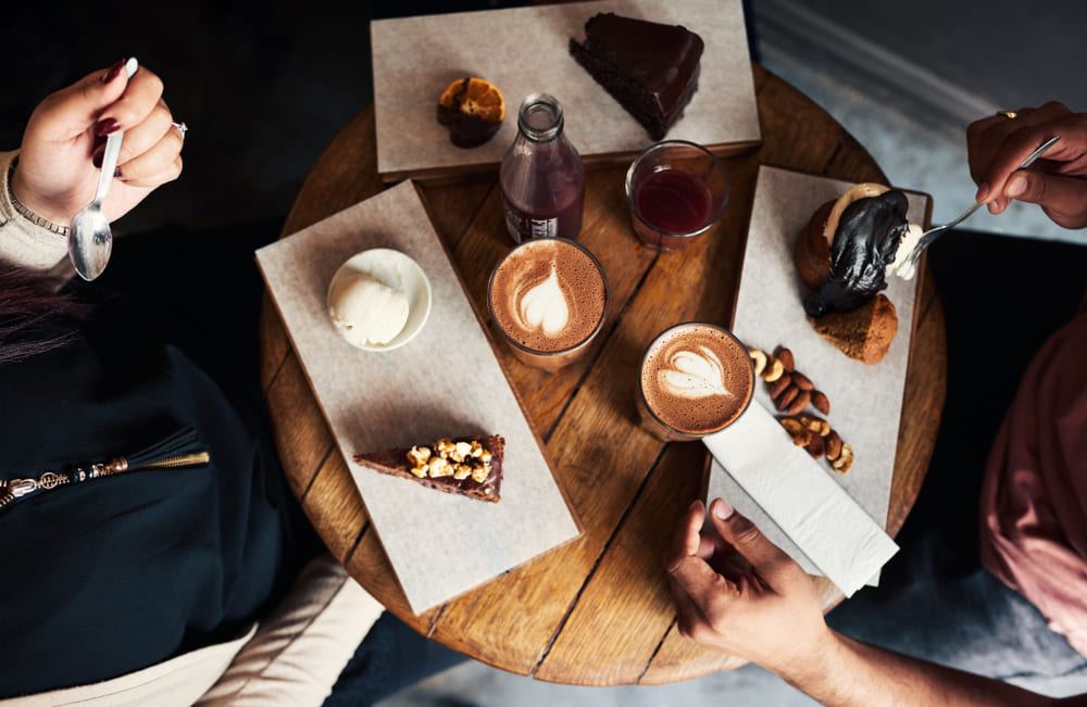 High angle of a diverse group of young friends sitting together around a cafe table enjoying an assortment of desserts and coffee