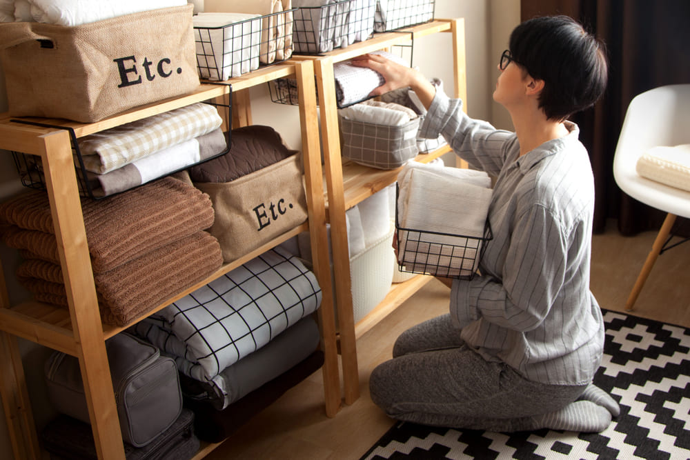 Spring cleaning of closet. Vertical tidying up storage. Neatly folded bed sheets in the metal black baskets for wardrobe. Nordic style.