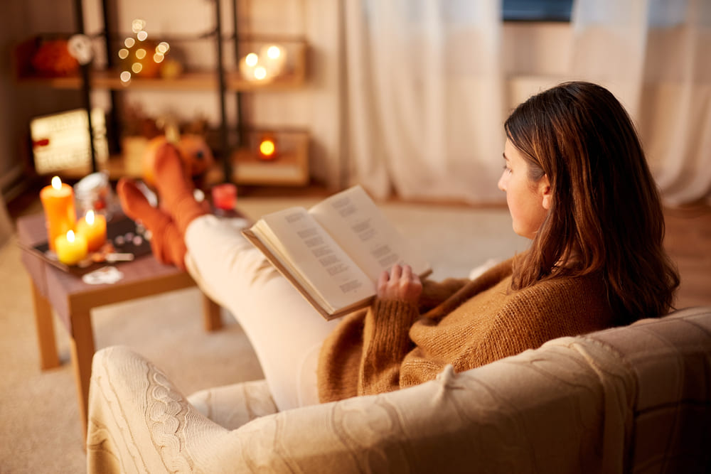  young woman reading book and resting her feet on table at cozy home